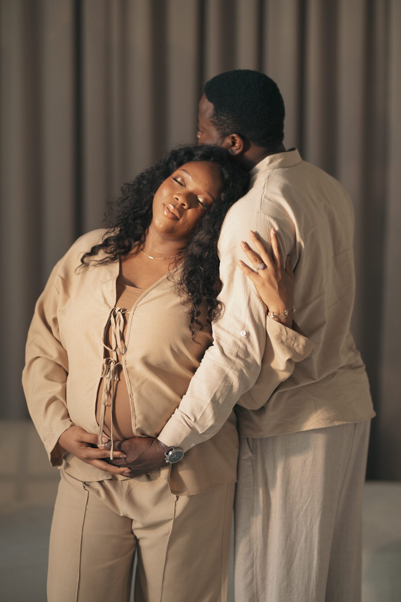 Expectant couple in cream, hands resting together