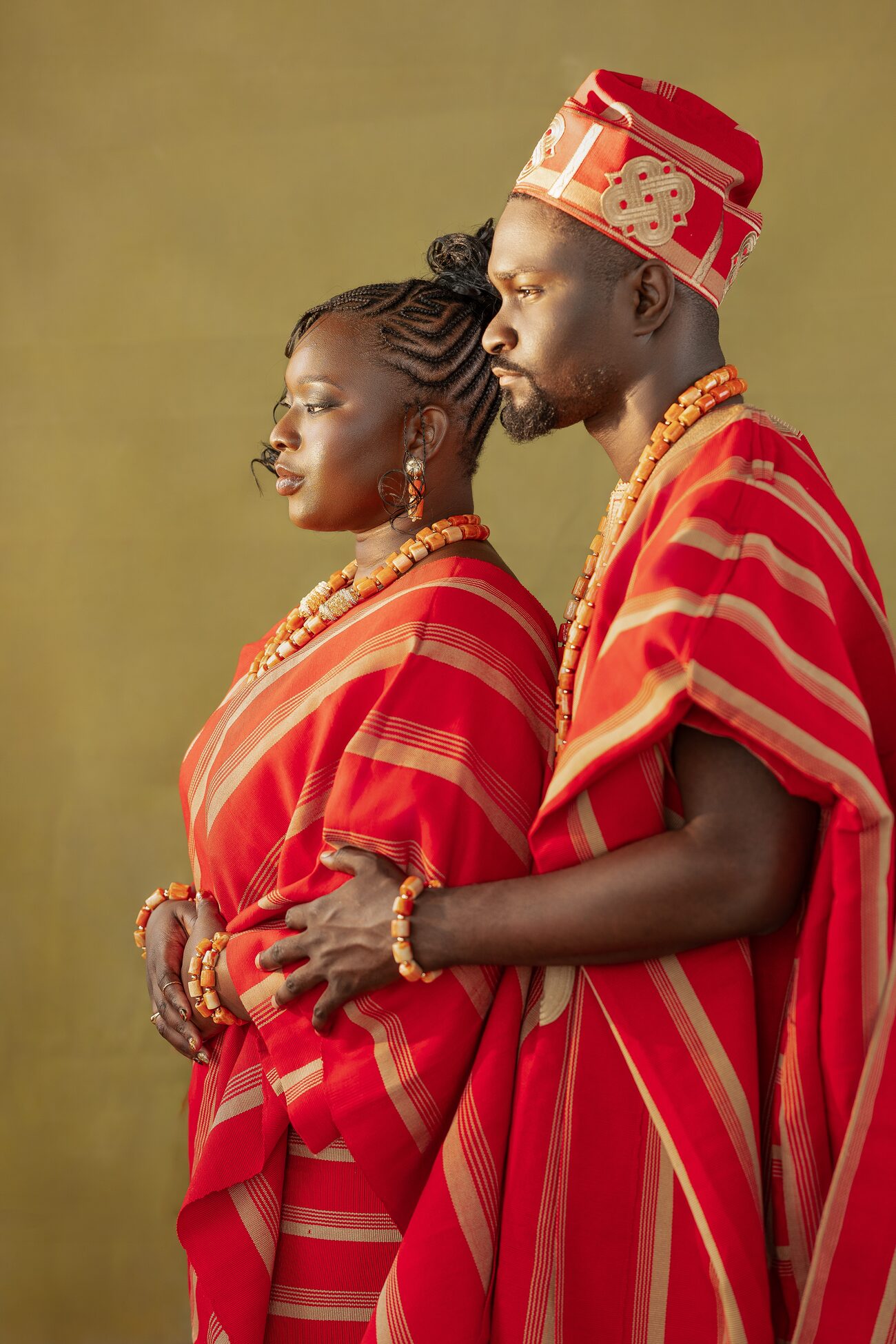 Couple in matching red and gold aso-oke, foreheads together